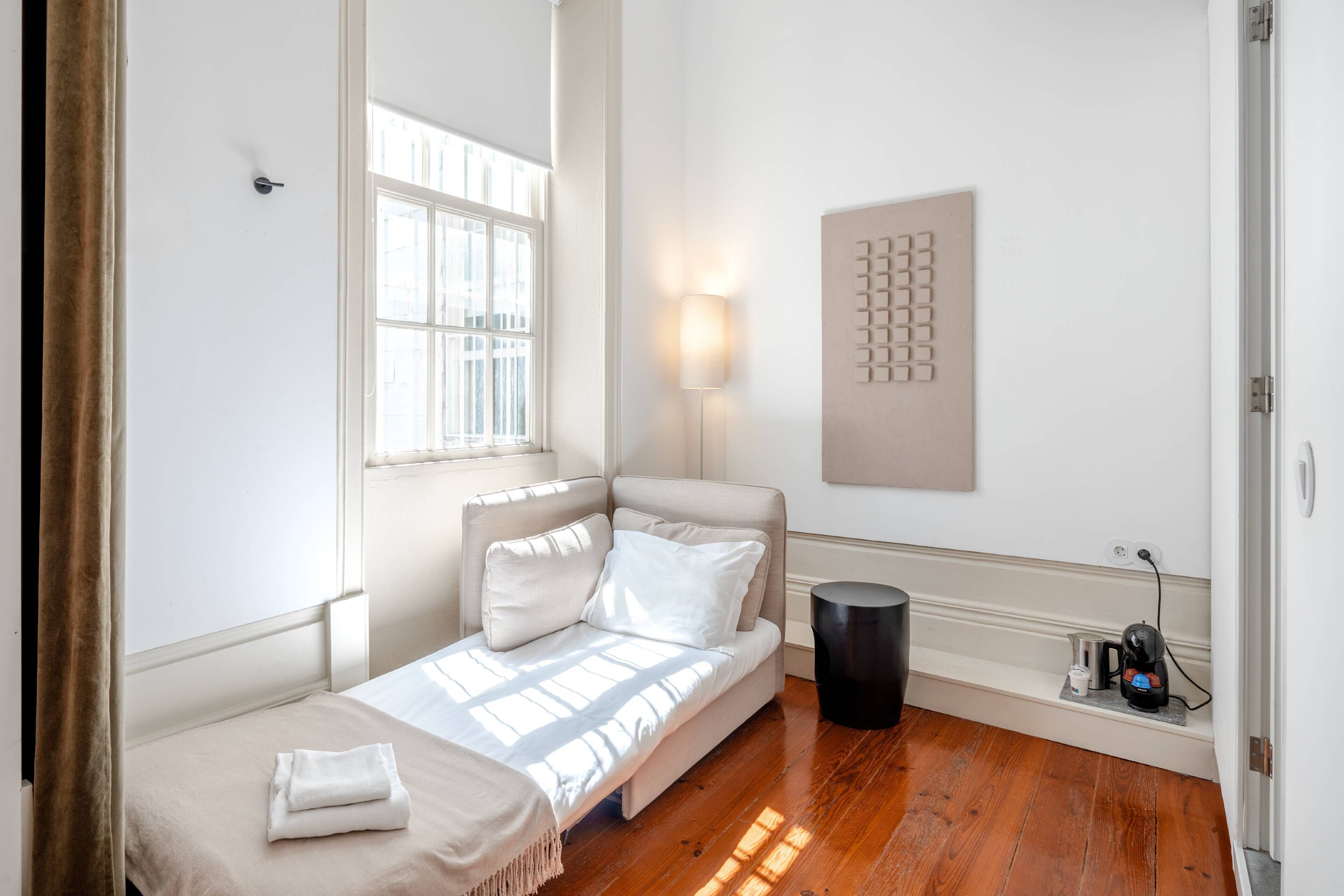 Quarto minimalista com cama, mesa de cabeceira, luminária e uma obra de arte pendurada na parede.