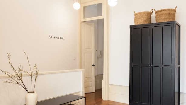 En gang med et sort skab, en hvid vase med grene, og et skilt der står "ALAMEDA".
