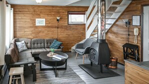 Una sala de estar acogedora con un sofá, un sillón y una chimenea. Se ve una escalera que sube a un nivel superior.