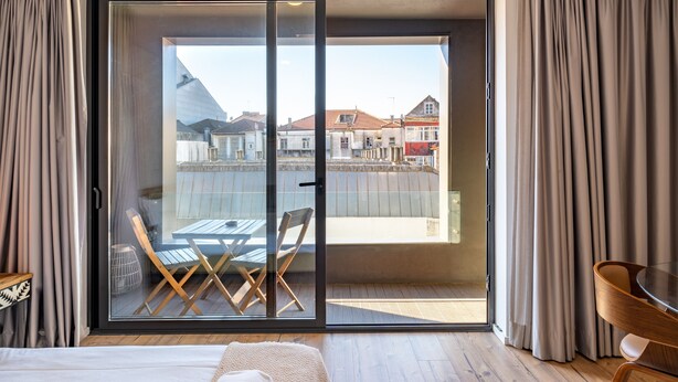 A hotel room with a large sliding glass door leading to an outdoor balcony with a table and chairs. - VIVA   In  the  MOOD (Porto)