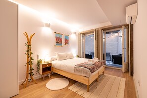 Un dormitorio con cama de madera, mesitas de noche, una planta en la mesita, un tapete redondo y vistas al exterior a través de una puerta corrediza.