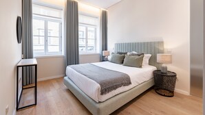 Ett modernt sovrum med en stor säng, sänglampor, ett litet sidobord och ett fönster med gardiner.
