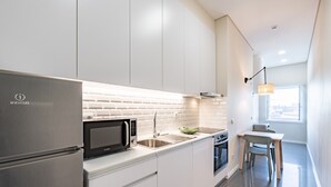 A modern kitchen with white cabinetry, a stainless steel refrigerator, a microwave, and a sink. - VIVA SIZE Flat Batalha - Apartment 2 (Porto)