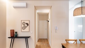 A hallway with a wooden floor, a table with two chairs, a framed artwork, and an air conditioning unit on the wall.