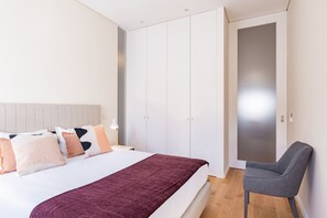 A modern bedroom with a bed, pillows, a chair, and a wardrobe.