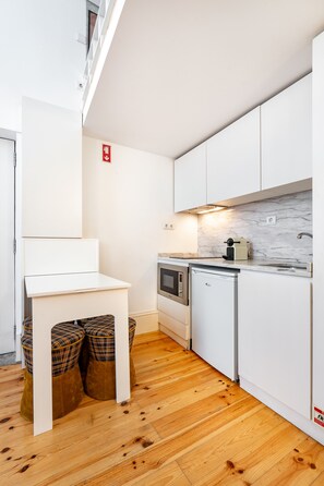 A compact kitchen with white cabinetry, a built-in oven, a microwave, and a coffee machine.