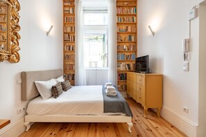 Ein ordentlich eingerichtetes Schlafzimmer mit einem Bett, Nachttischen, einem Fernseher und einem Bücherregal voller Bücher.
