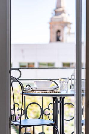 A balcony with a table set for two, a clear glass, and a view of a building with a tower.