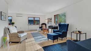 A modern living room with a sofa, armchair, and ottoman, a dining table with a candle, and a large window with a view of greenery.