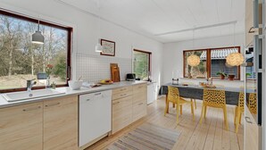 A modern kitchen with wooden cabinets, a dishwasher, and a large window overlooking a forest.