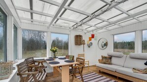 A spacious room with a large table and chairs, a sofa, and a view of the outdoors through large windows.