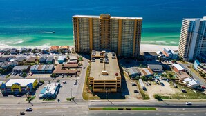 A high-rise hotel with a central parking lot, beachfront view, and adjacent smaller buildings.