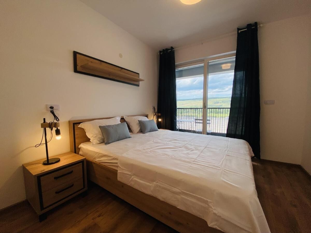 Un dormitorio con una cama grande, una mesita de noche, cortinas en la ventana y vistas al exterior.
