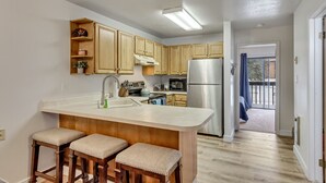 A modern kitchen with wooden cabinets, a stainless steel refrigerator, and a built-in island with bar stools. - Charming condo w/ king bed, hot tub, pool, minutes away from world class skiing (Eden)