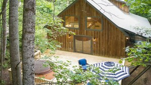 Una cabaña de madera con un gran ventanal corredera, una terraza con mobiliario exterior y un techo de metal.
