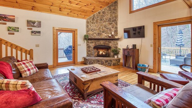 Una sala de estar acogedora con chimenea de piedra, techo de madera y ventanas amplias.