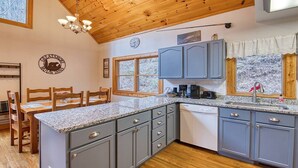 Una cocina con encimeras de granito, gabinetes grises, techo de madera y un comedor con sillas y mesa de madera.
