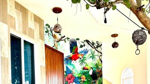 Une pièce avec deux chaises, une porte en bois, une fresque murale colorée, un escalier et une plante en pot.