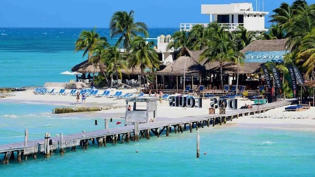 Un hôtel situé en bord de mer, doté d’une jetée, de parasols de plage et de palmiers.