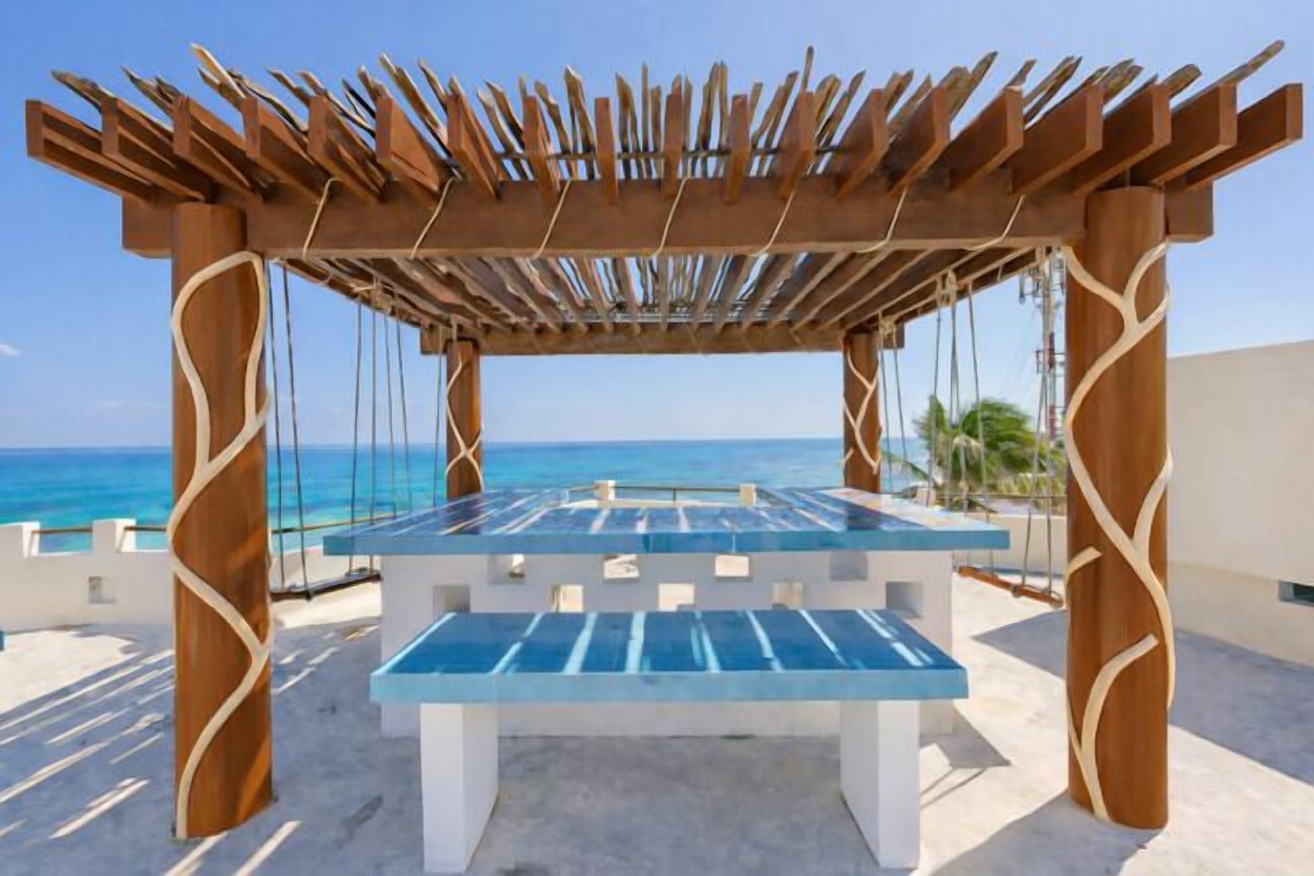 Eine Holz-Pergola mit Glastisch und Bänken, mit Blick auf einen Strand.