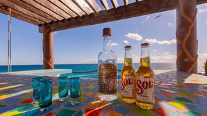 A table with a colorful mosaic tablecloth, a bottle of tequila, and two bottles of Sol beer, set against a view of the ocean. - Casa Cielo Studio 2 with detached Bayview Balcony (Isla Mujeres)