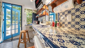 A kitchen with blue and white patterned tiles, a wooden stool, a TV mounted on the wall, and a door with blue shutters. - Casa Cielo Studio 2 with detached Bayview Balcony (Isla Mujeres)