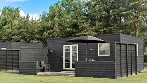 Una cabaña moderna de color oscuro con un área de patio, una puerta y una ventana.