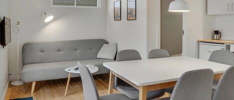 Een moderne woonkamer met een grijze bank, een ronde eettafel en grijze stoelen. Er is een raam met uitzicht op bomen en een schilderij aan de muur.