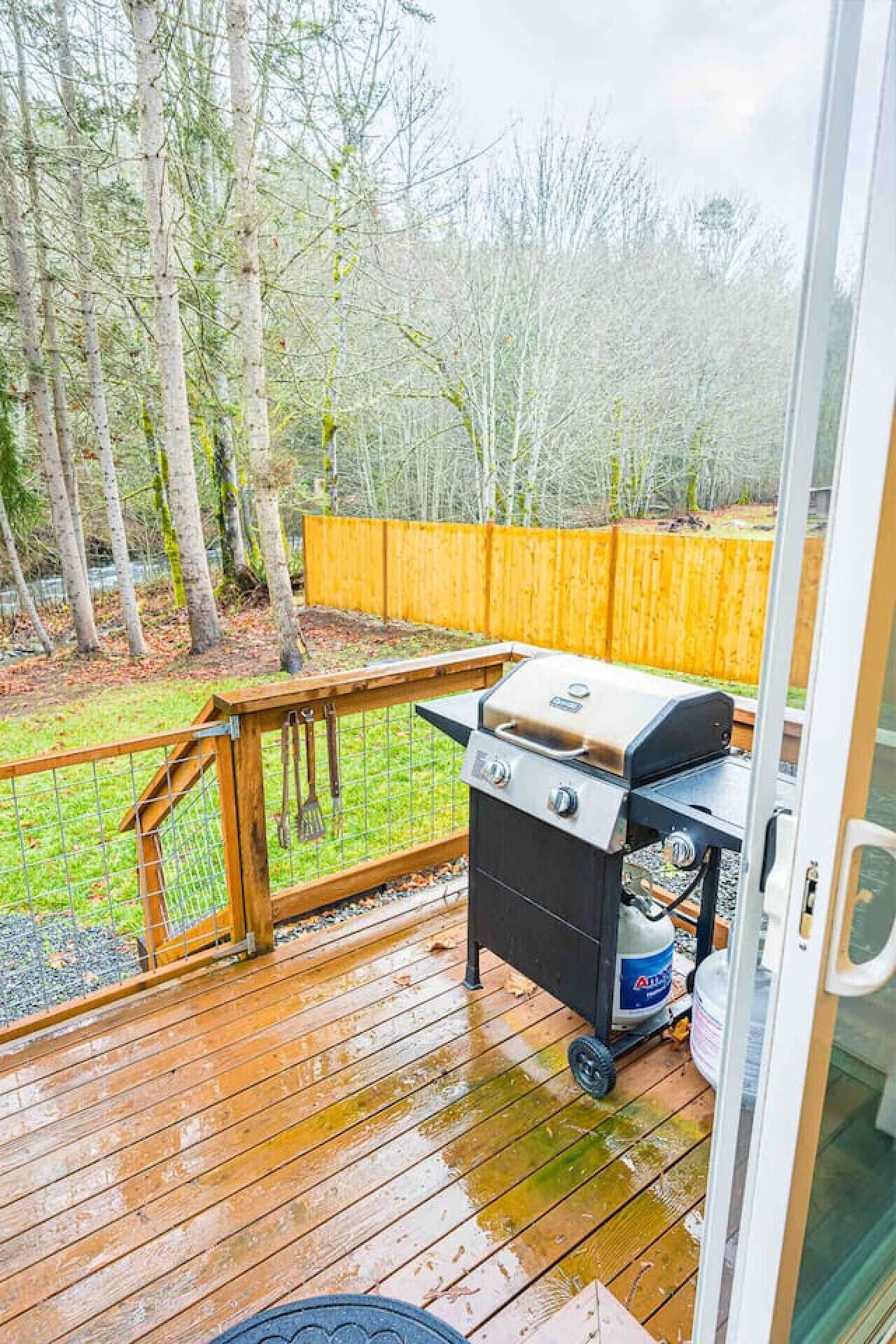 Eine Terrasse im Freien mit einem Grill, einem Holzzaun und einem Rasen.