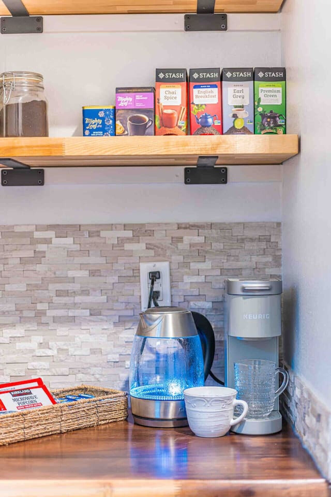 En köksbänk med en kaffebryggare, en vattenkokare och en mikrovågsugn. På hyllan ovanför står det kartonger med Stash-te.