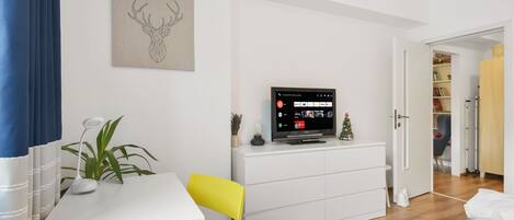 A modern bedroom with a white dresser, a yellow chair, a TV on the dresser, and a door leading to another room.