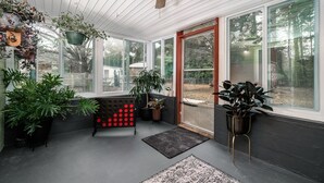 Une véranda avec un ventilateur de plafond, de grandes fenêtres et diverses plantes en pot.