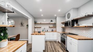Une cuisine moderne avec des meubles blancs, des plans de travail en bois et un revêtement mural en carreaux. Elle est équipée d’appareils électroménagers intégrés, notamment un four à micro-ondes et un four traditionnel, ainsi que d’un évier avec un robinet.