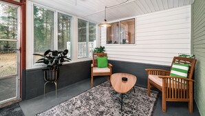 Une véranda avec de grandes fenêtres, un ventilateur de plafond et deux fauteuils en bois avec des coussins.