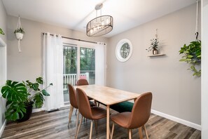 A dining area with a wooden table and brown chairs, a hanging light fixture, and potted plants.