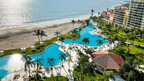 A resort with a large pool area, palm trees, and a beach view.