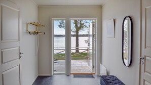 Et værelse med bænk, spejl og udsigt over en sø gennem en glasdør.