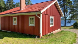 Et rødt træhus med skråt tag, to vinduer og en skorsten.