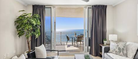 A balcony with a view of the sea, a ceiling fan, a sofa, a chair, a table, and a potted plant.