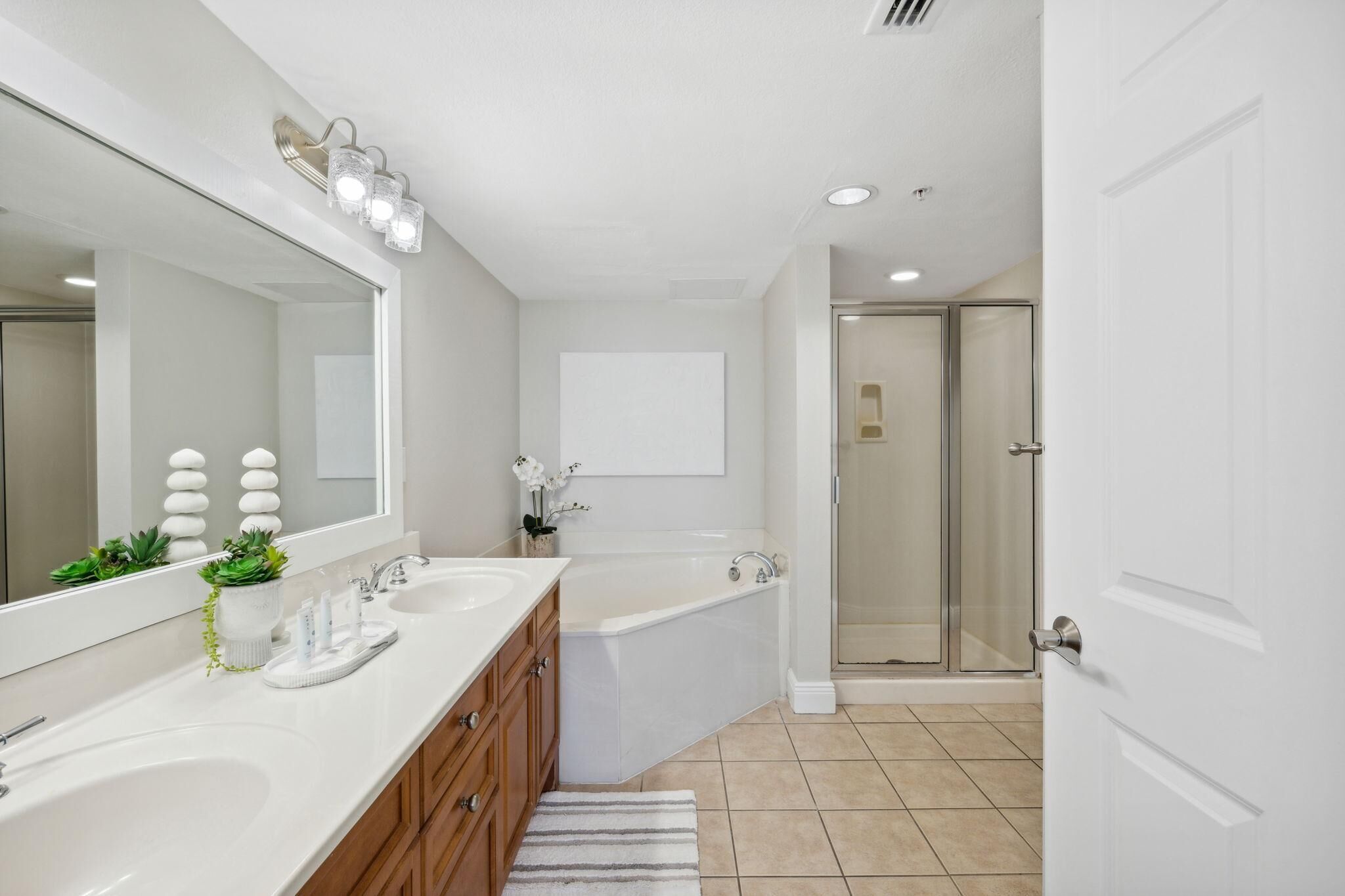 A modern bathroom with two sinks, a large mirror, a bathtub, and a walk-in shower.