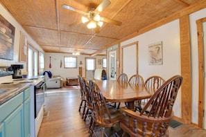 A spacious dining area with a wooden table and chairs, a ceiling fan, and a kitchen area with a stove and cabinets.