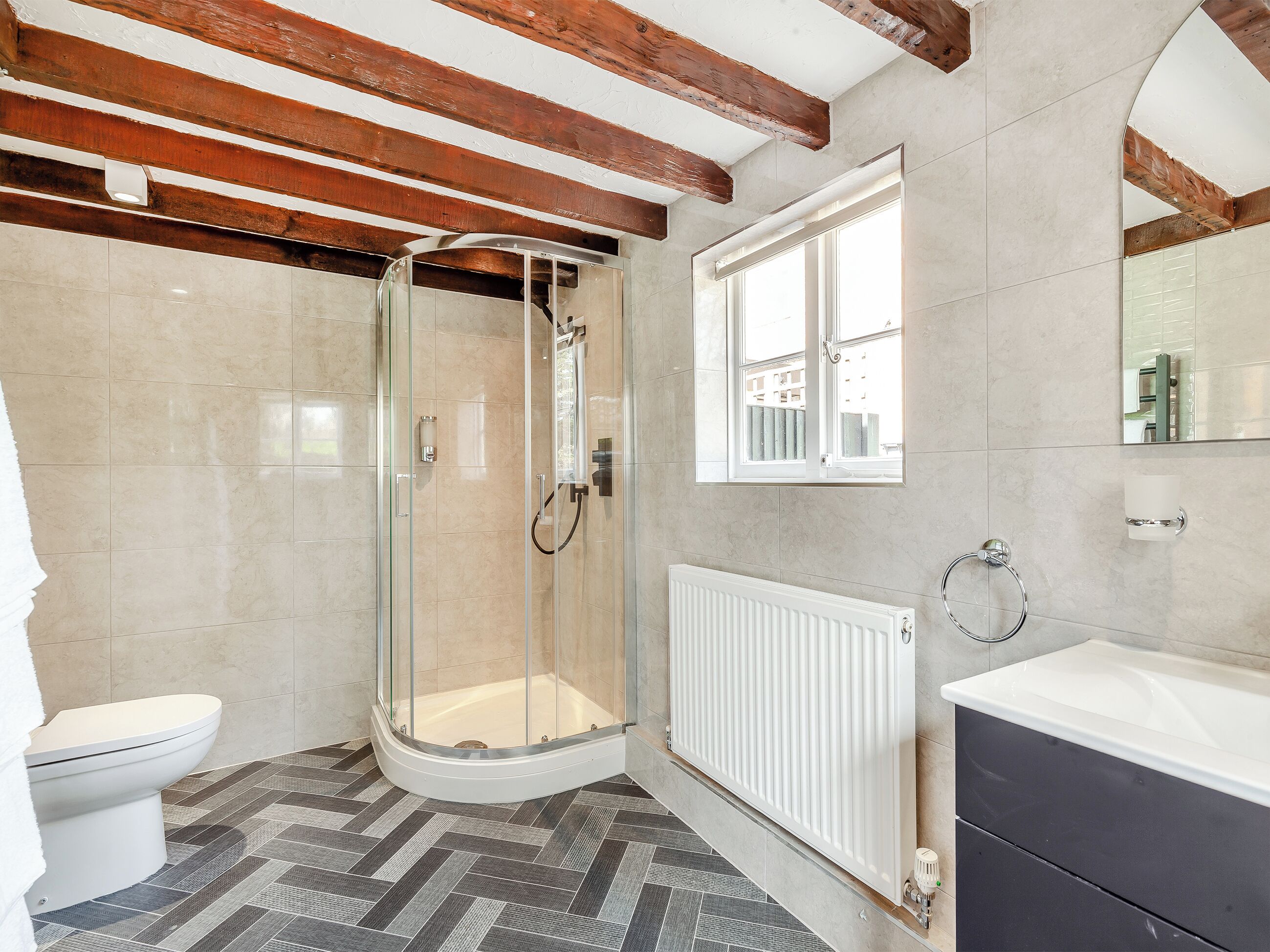 Une salle de bain équipée d’une douche, de toilettes et d’une baignoire, avec un sol au motif en chevrons et des poutres apparentes.