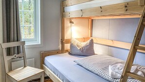 A bunk bed with a checkered pillow and a bedside lamp, a wooden chair, and a window with curtains. - Gorgeous home in Offersøy with sauna (Offersøy)