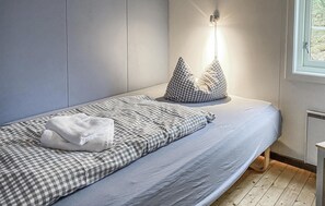 A modern bedroom with a single bed, checkered bedding, a bedside lamp, and a window with a view of trees. - Gorgeous home in Offersøy with sauna (Offersøy)