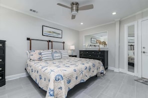 A bedroom with a bed, a ceiling fan, a nightstand, a dresser, a mirror, and a door.