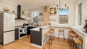 A modern kitchen with a central island, bar stools, and a view of the city through large windows. - Cream City Victorian Parking AC Patio Walkable (Milwaukee)