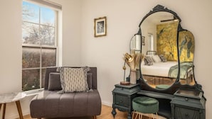A room with a large window, a sofa, a vanity with a mirror, and a bed. - Cream City Victorian Parking AC Patio Walkable (Milwaukee)