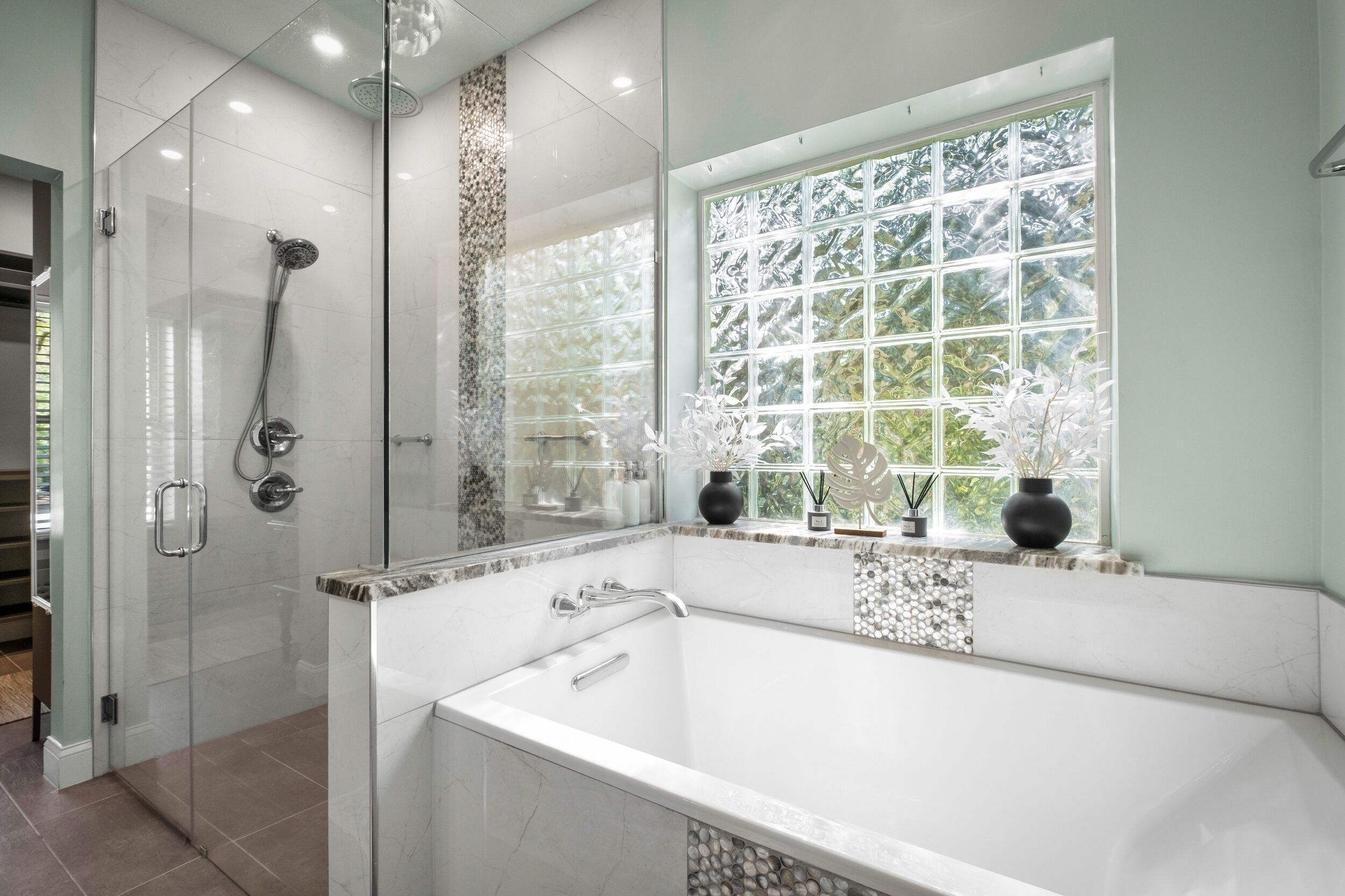 Une salle de bain moderne avec une douche à l’italienne, une grande baignoire et une fenêtre donnant sur la verdure.