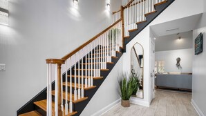 Un escalier moderne avec des marches en bois et des balustrades blanches, menant à un espace de vie comprenant un canapé et une plante.