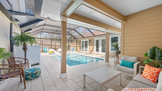 Un patio couvert avec une piscine, des meubles d’extérieur et des plantes en pot.